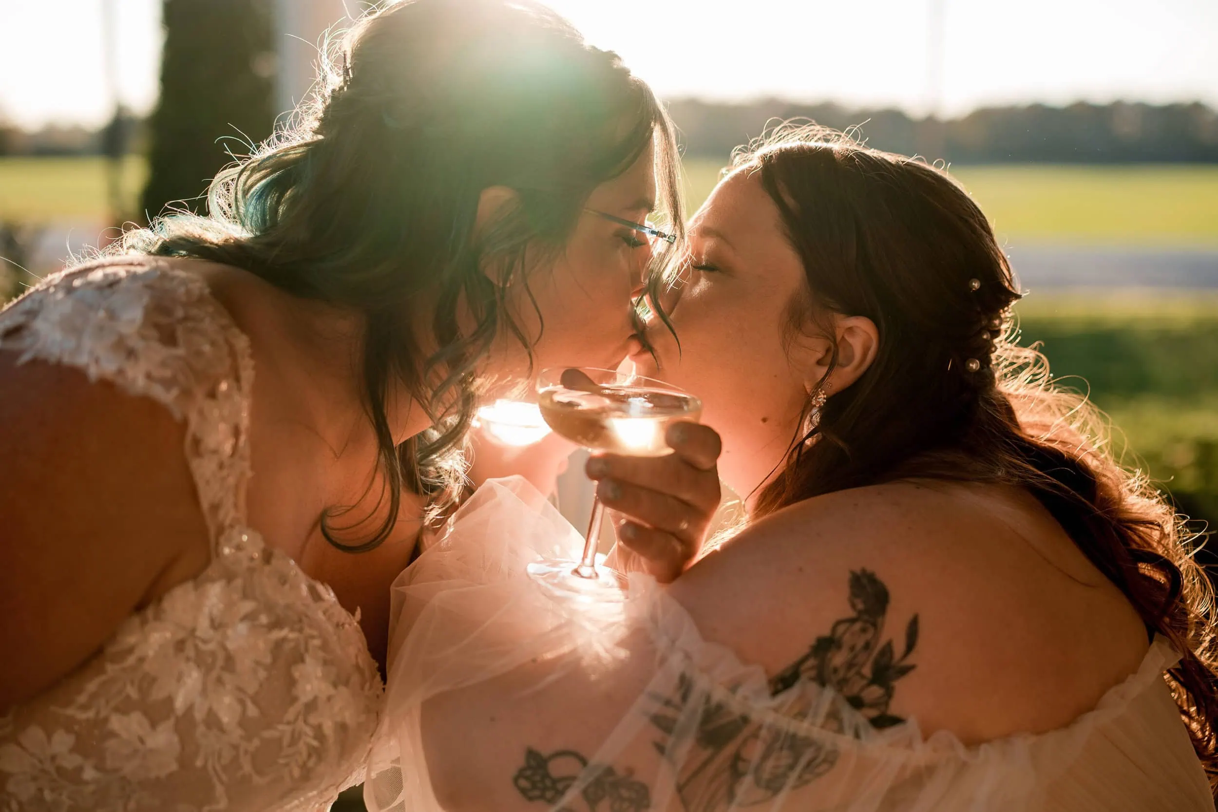 lgbtq2+ brides kissing with champagne glasses in golden hour light